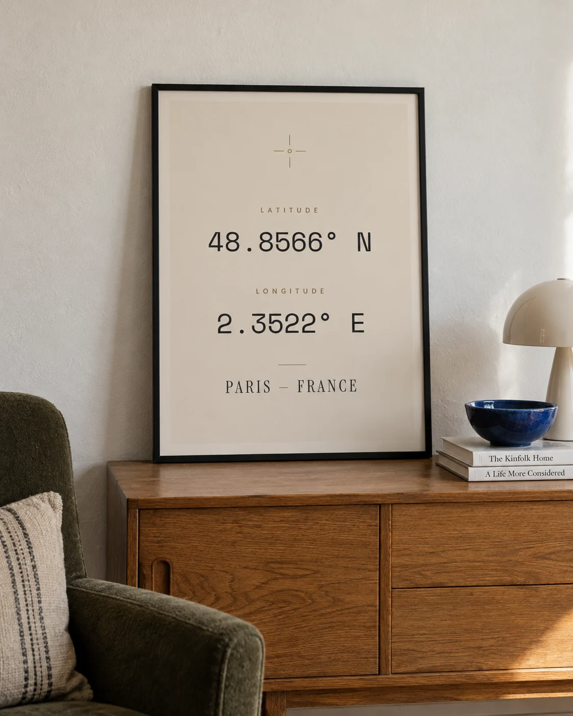 Sandfarbenes Paris-Koordinatenposter im schwarzen Rahmen auf einem Eichen-Sideboard neben einem Lesesessel.